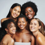 Beauty portrait of a diverse group of beautiful women smiling together against a grey studio background. Faces of female models with perfect, clear skin and complexion from a daily skincare routine
